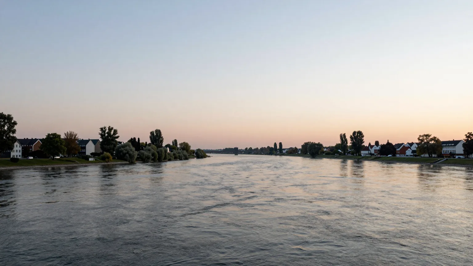 Breites Flussufer mit Bäumen und Häusern im Morgenlicht
