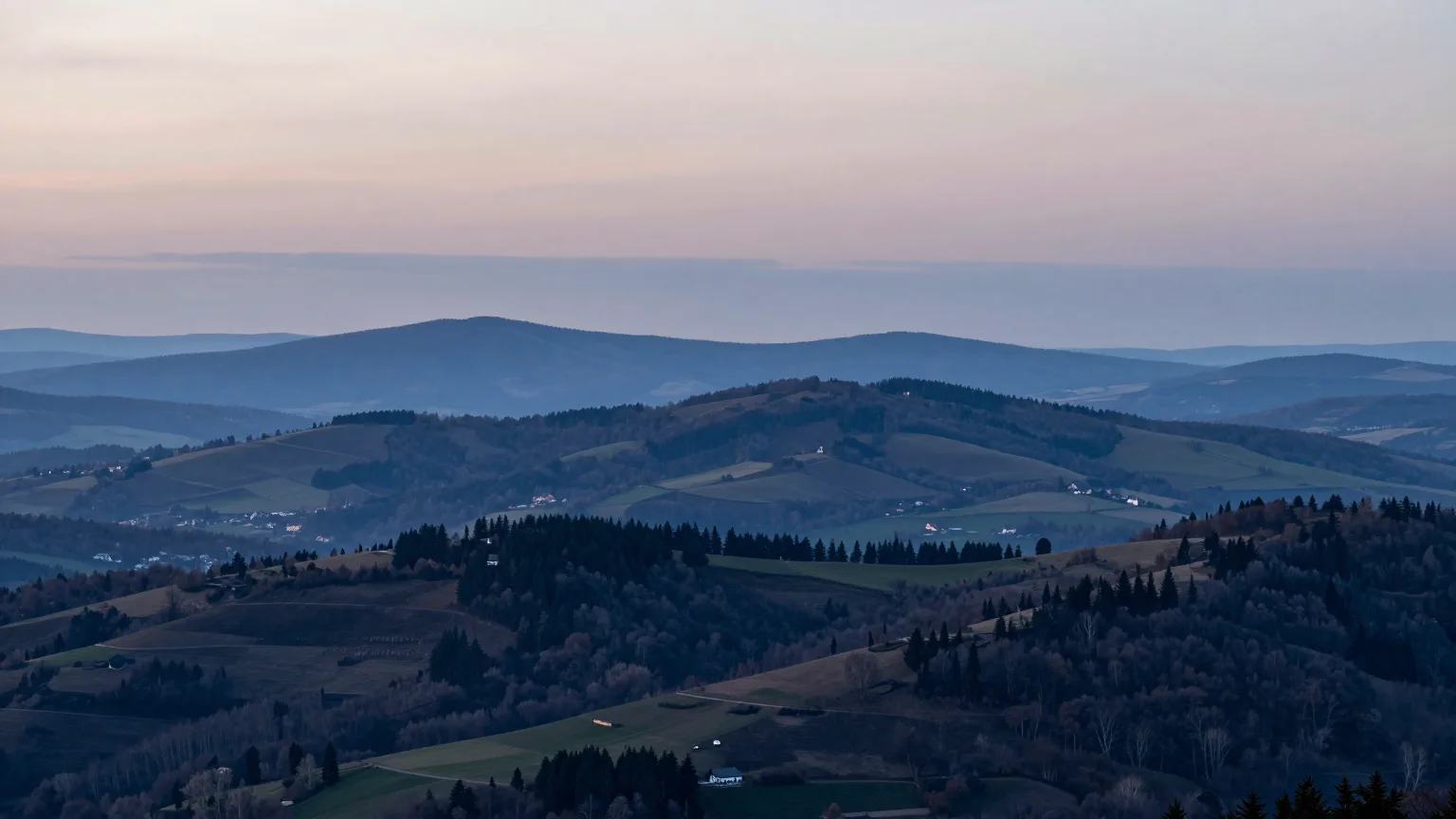 Hügellandschaft mit Feldern, Wald und einer Fernstraße im Abendlicht