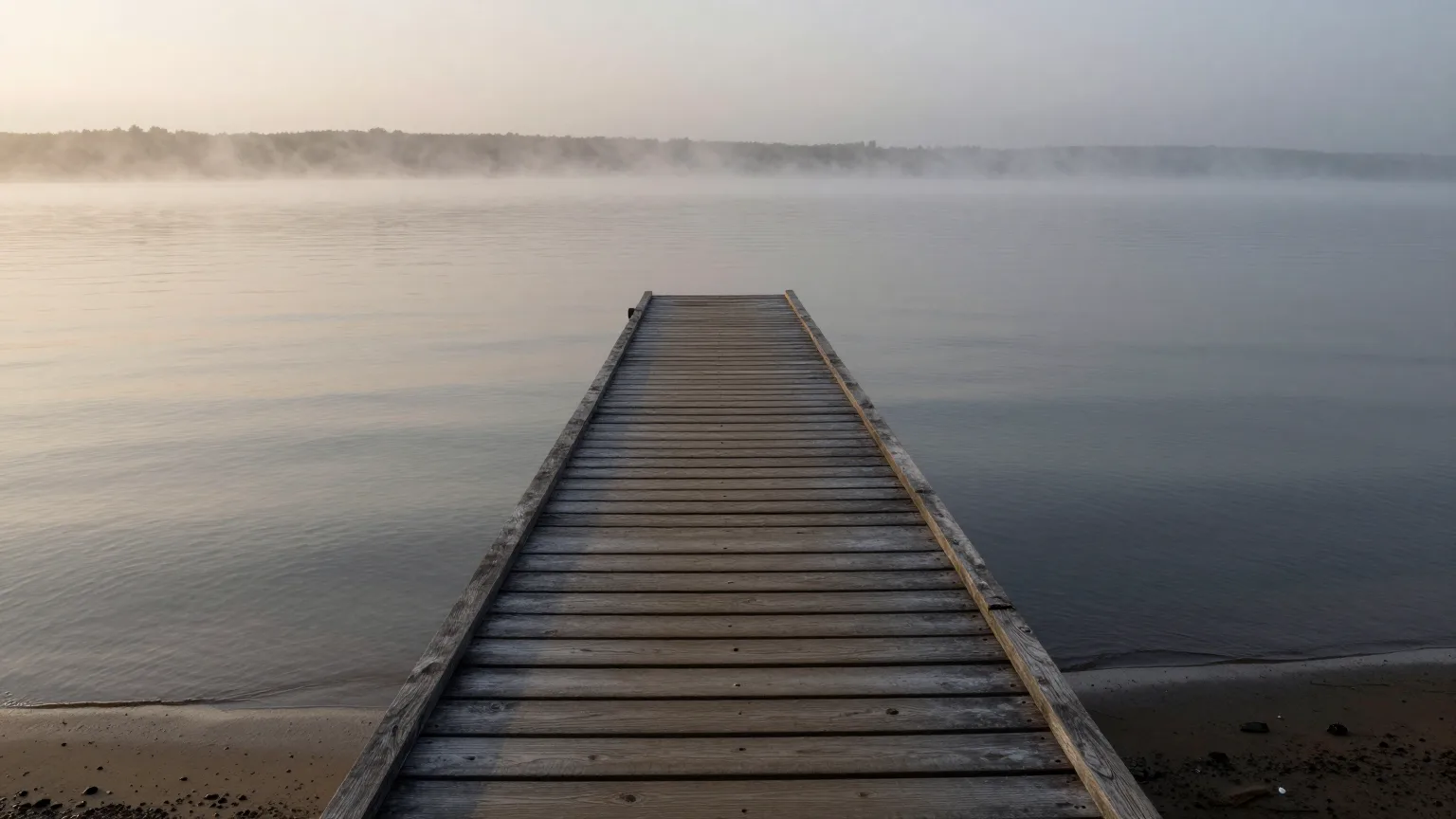 Holzsteg, der im Morgennebel auf einen stillen See hinausführt